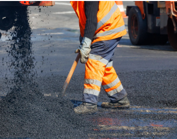 A worker in high-visibility gear using a tool to spread asphalt during roadway paving services, highlighting Morris Town Paving's professional road construction expertise in Morris County, NJ.